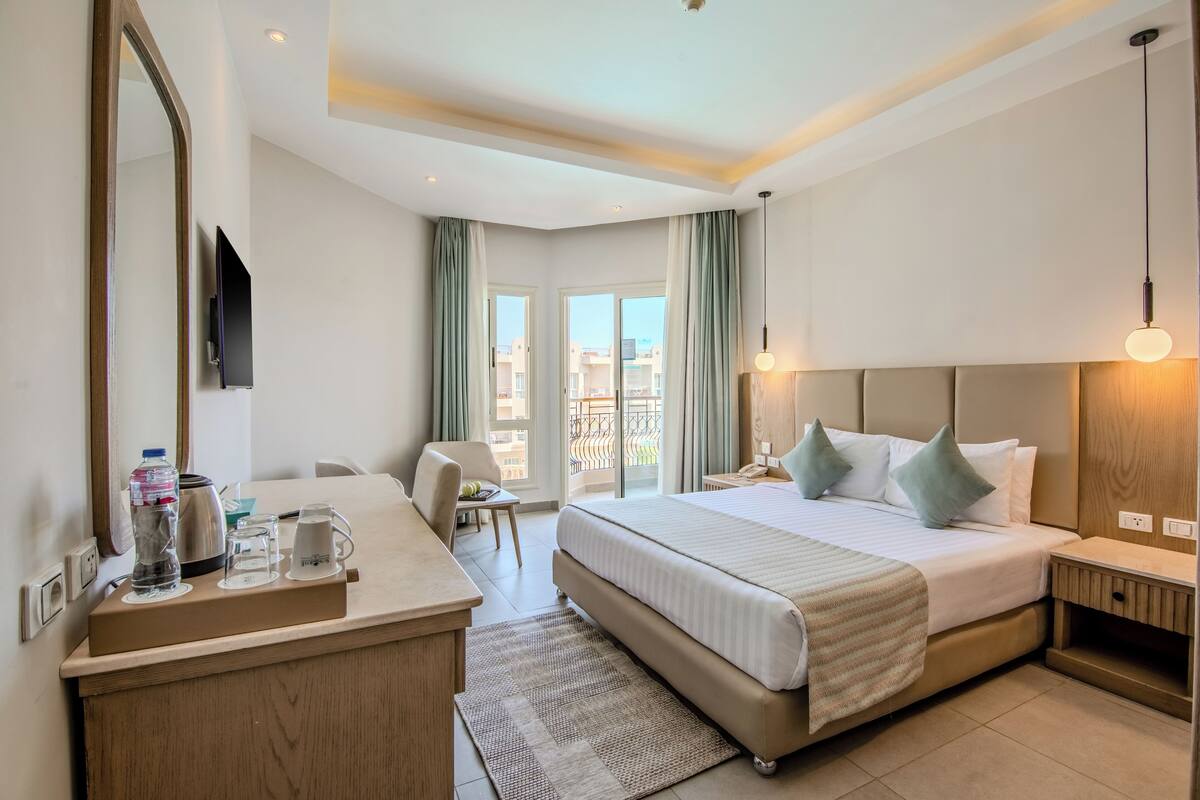 Une chambre d’hôtel moderne dotée d’un grand lit, d’un bureau avec un miroir, d’une télévision à écran plat et offrant une vue sur la ville grâce à de grandes fenêtres.
