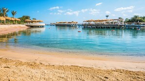 A beach with clear blue water, a pier with thatched-roof structures, and a sandy shore.