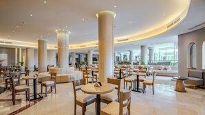 A spacious lobby with multiple seating areas, including round tables and sofas, and large pillars.