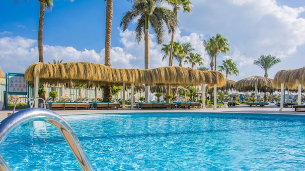A swimming pool with thatched umbrellas, palm trees, and lounge chairs.