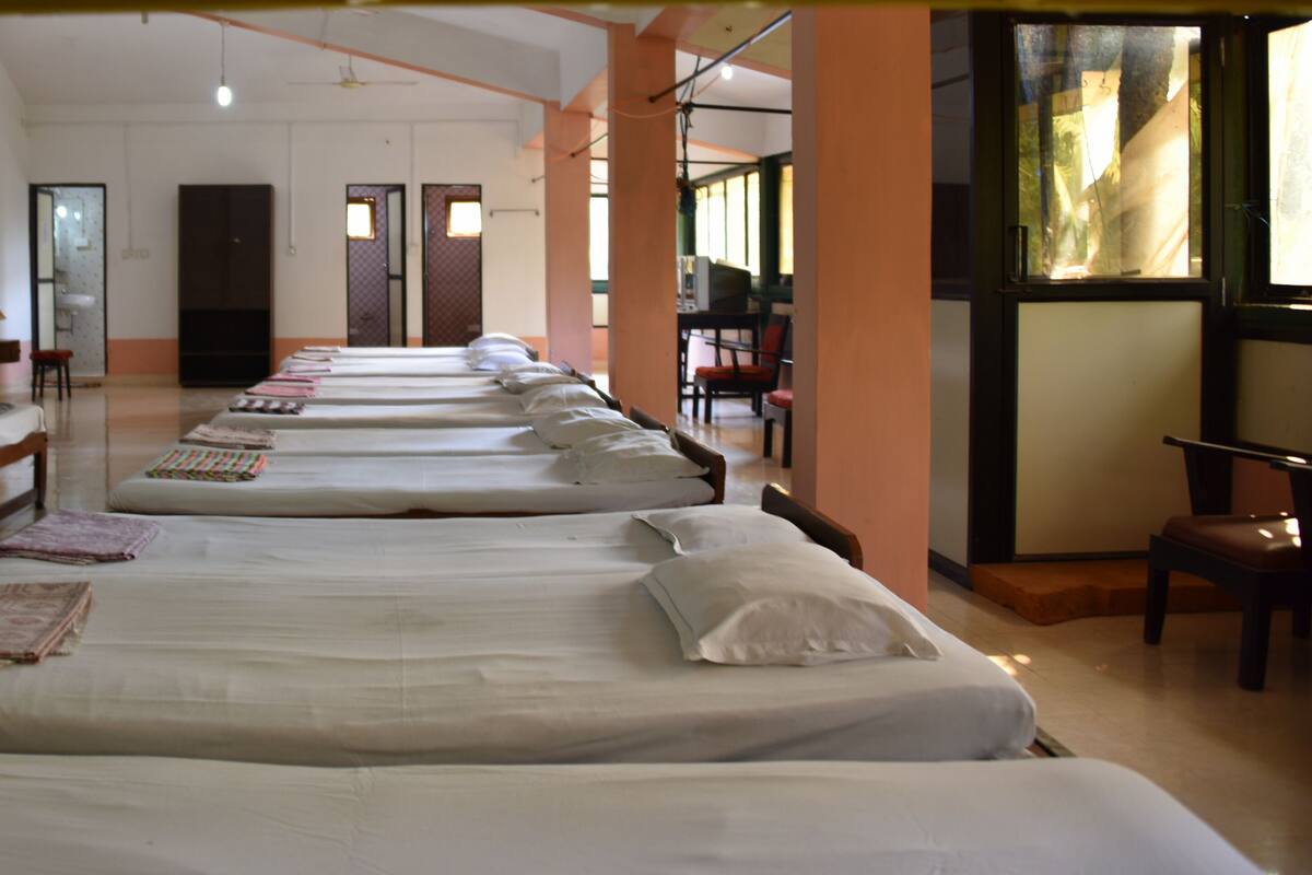 Quarto de hotel com várias camas alinhadas, uma televisão e uma escrivaninha com uma cadeira.