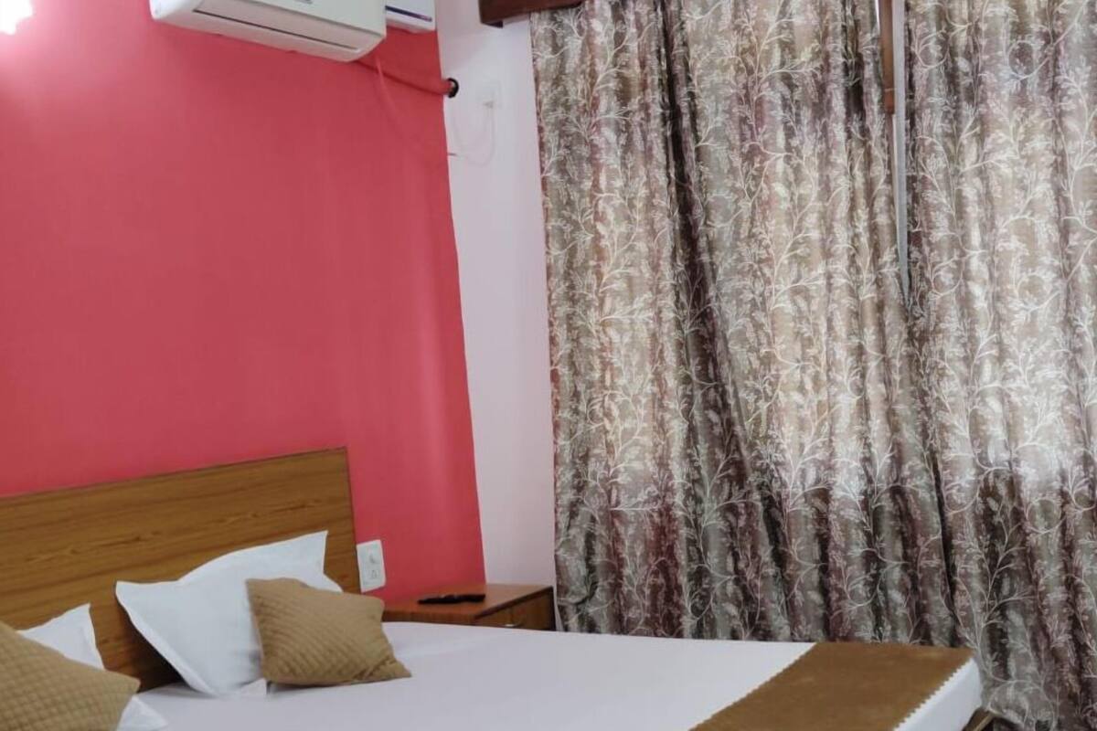 Cama com cabeceira de madeira, roupa de cama branca e dois travesseiros bege.