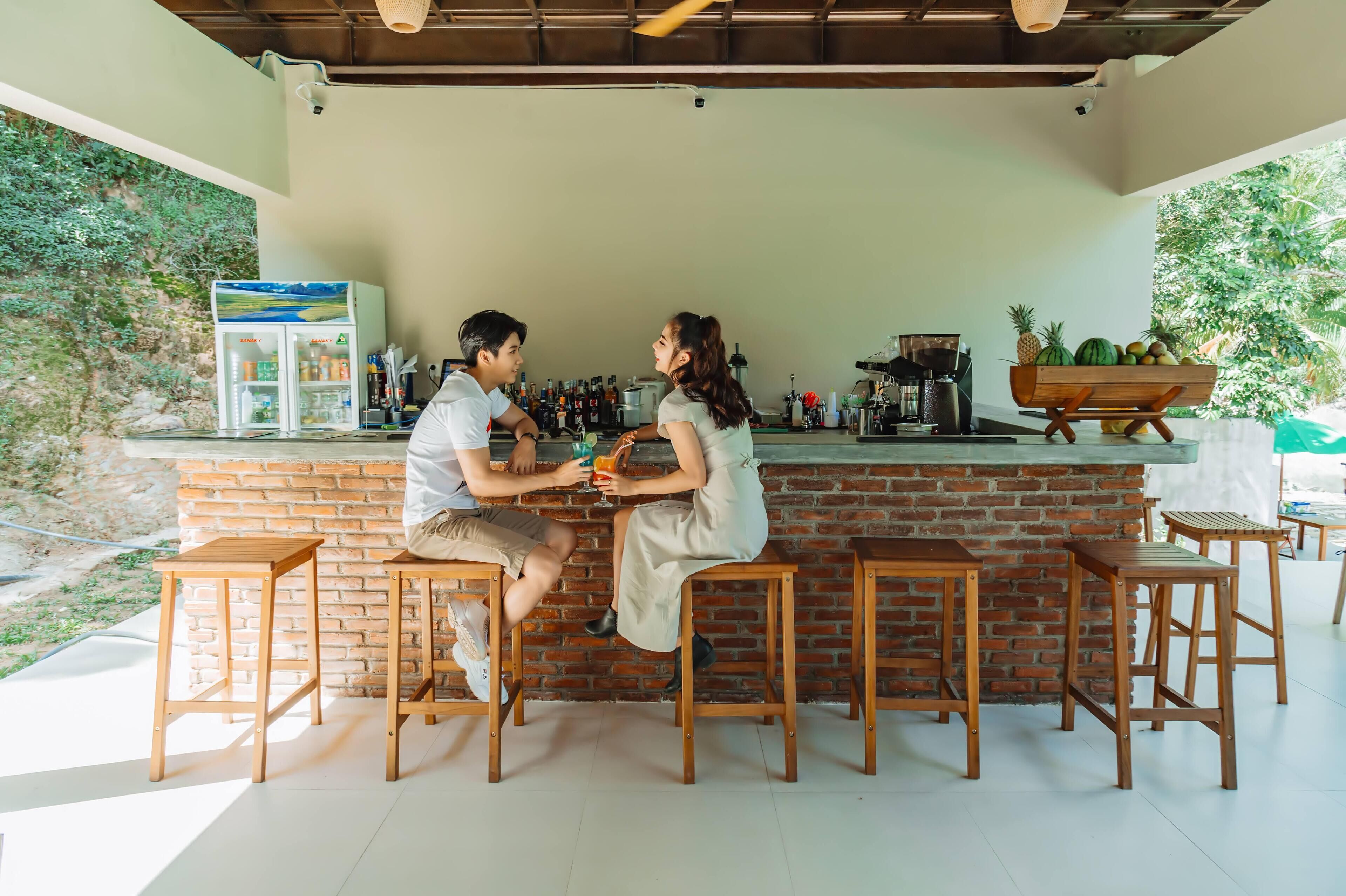 A bar area with wooden stools, a brick counter, and a refrigerator stocked with beverages.