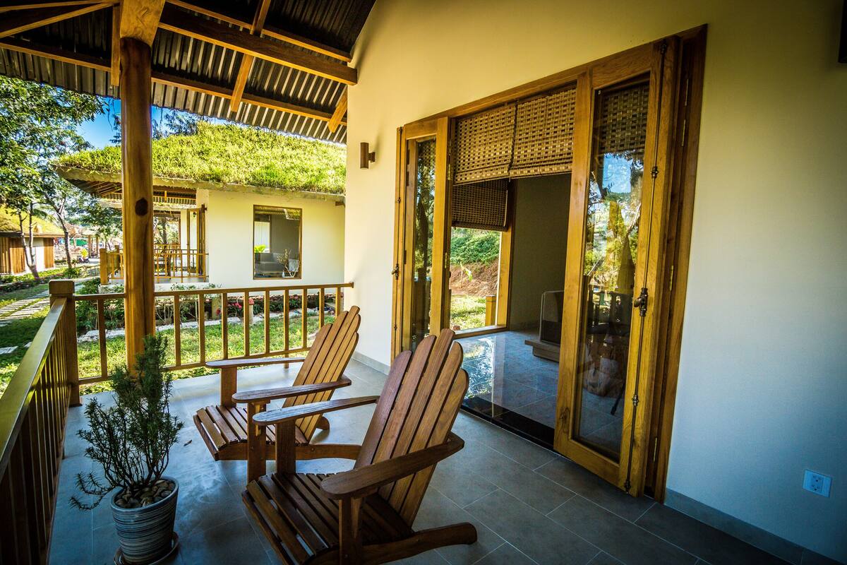 A wooden deck with rocking chairs and a potted plant, leading to a glass door entrance.