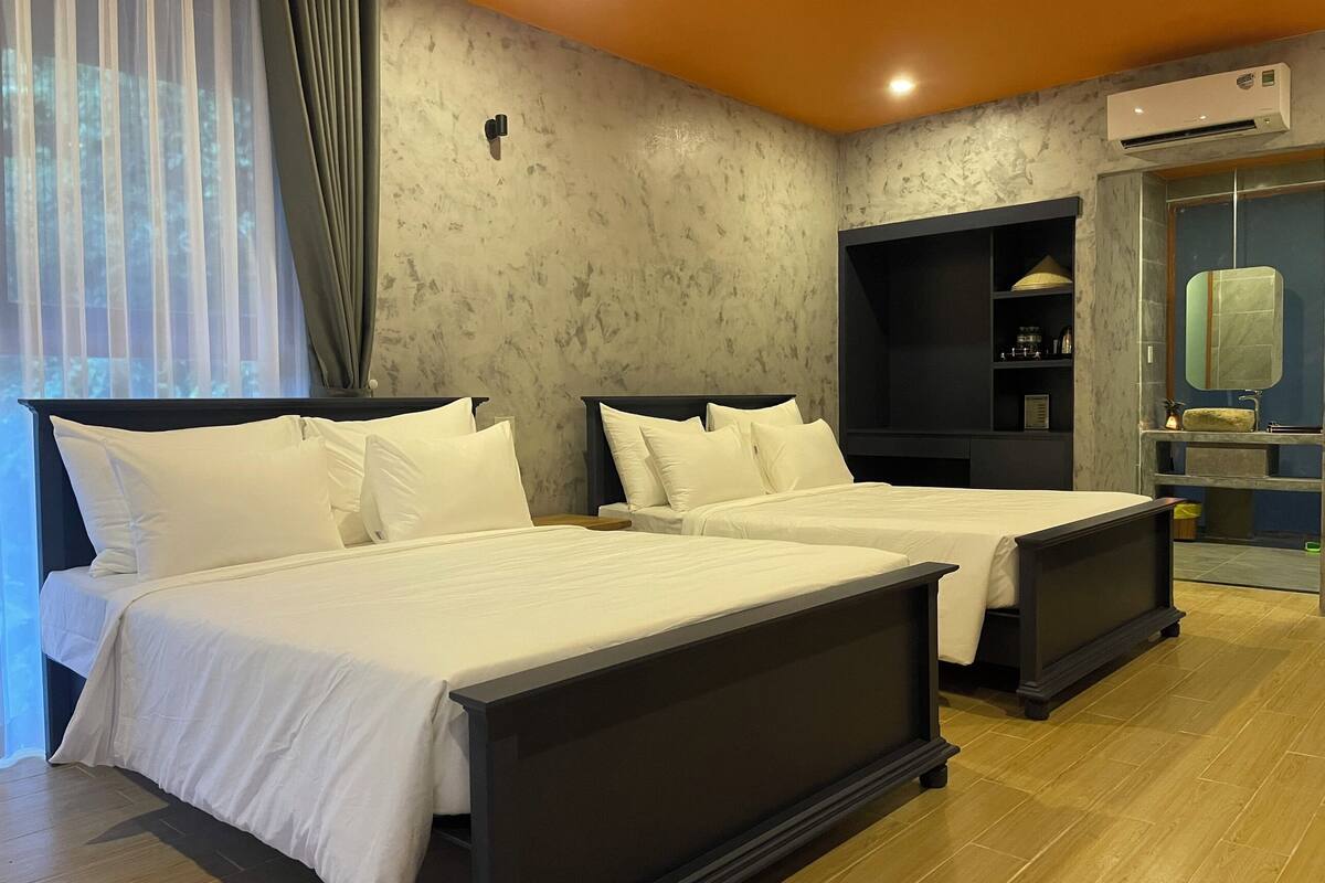 A hotel room with two beds, a built-in shelf, an air conditioning unit, and a bathroom with a mirror and sink.