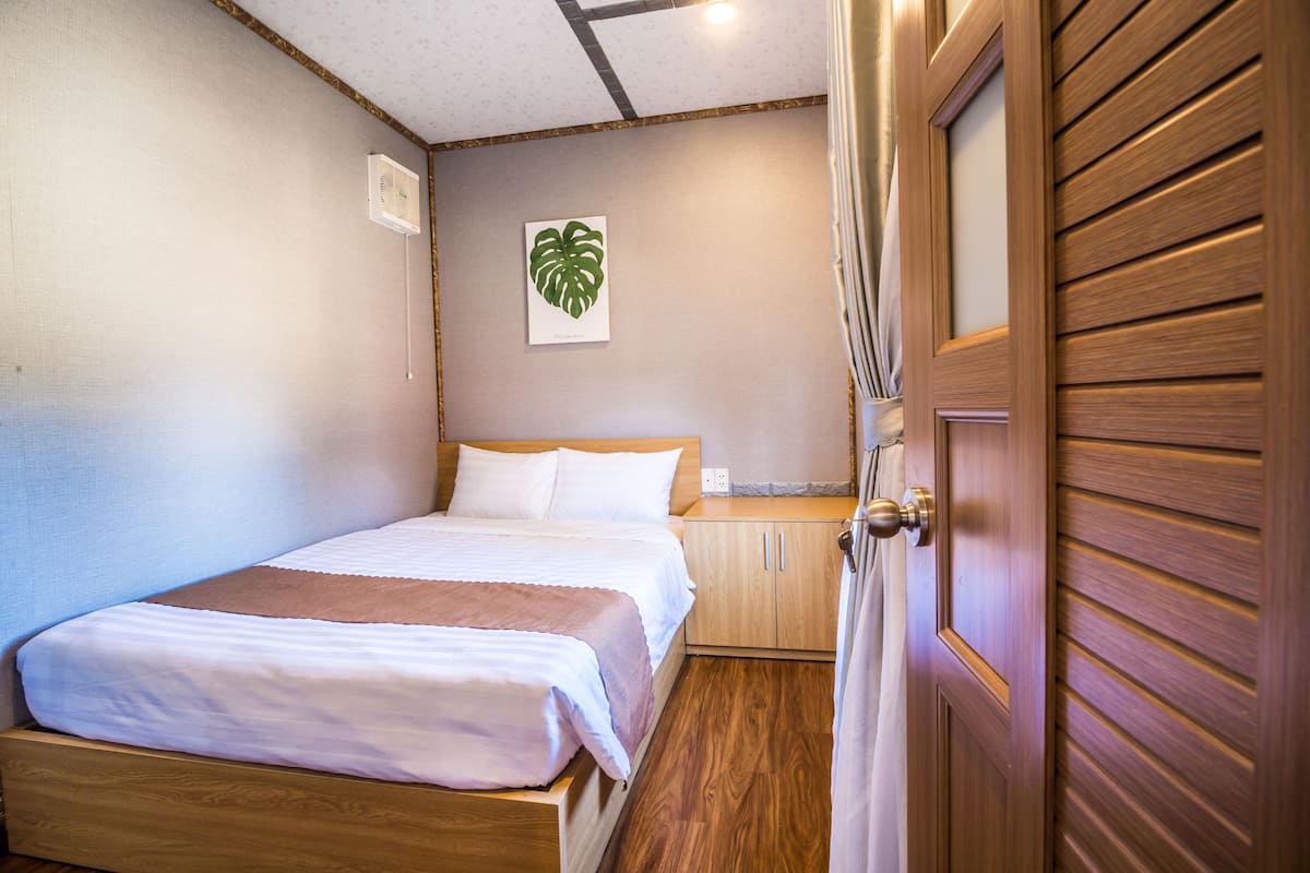 A bedroom with a wooden bed, a nightstand, a wooden wardrobe, and a ceiling light fixture.