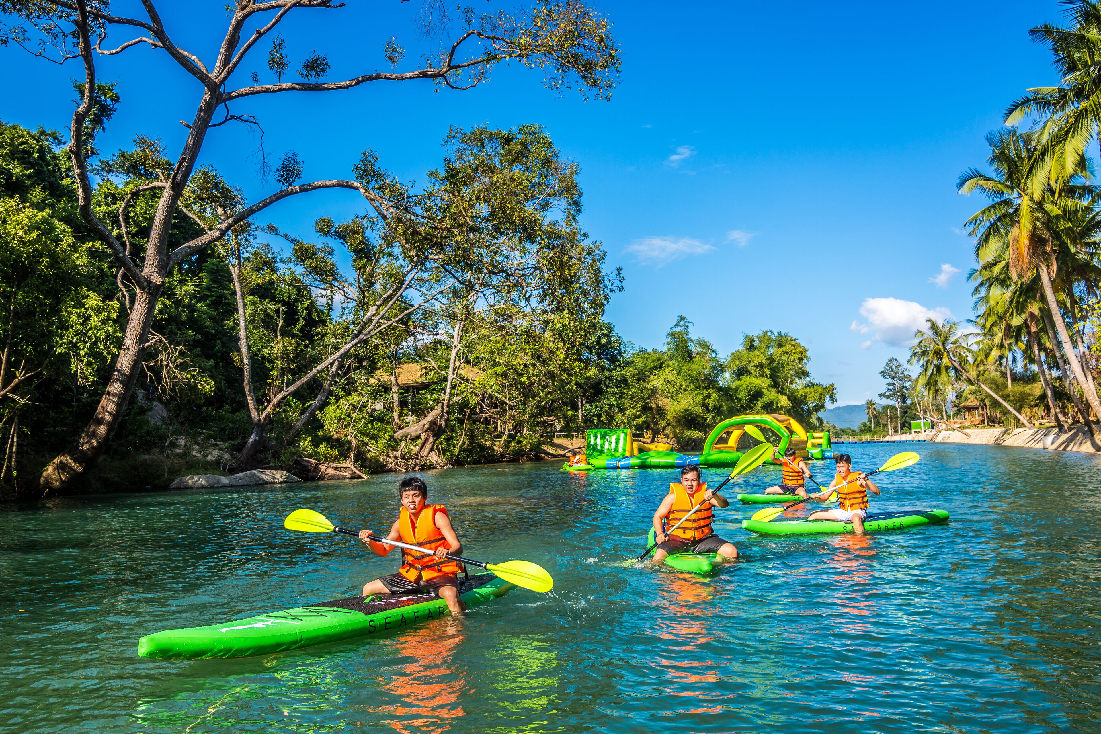 A group of people kayaking on a river surrounded by lush greenery and palm trees.