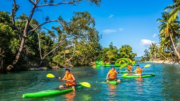 A group of people kayaking on a river surrounded by lush greenery and palm trees.