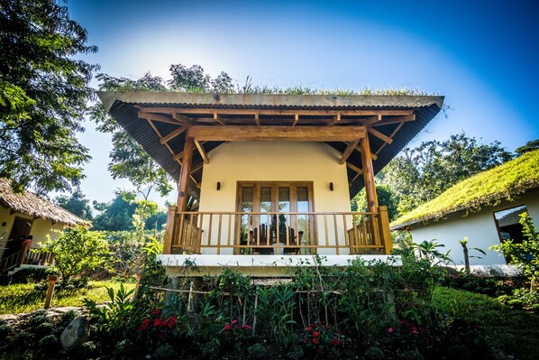 Un edificio de estilo tradicional con un balcón de madera, rodeado de exuberante vegetación y un cielo despejado.