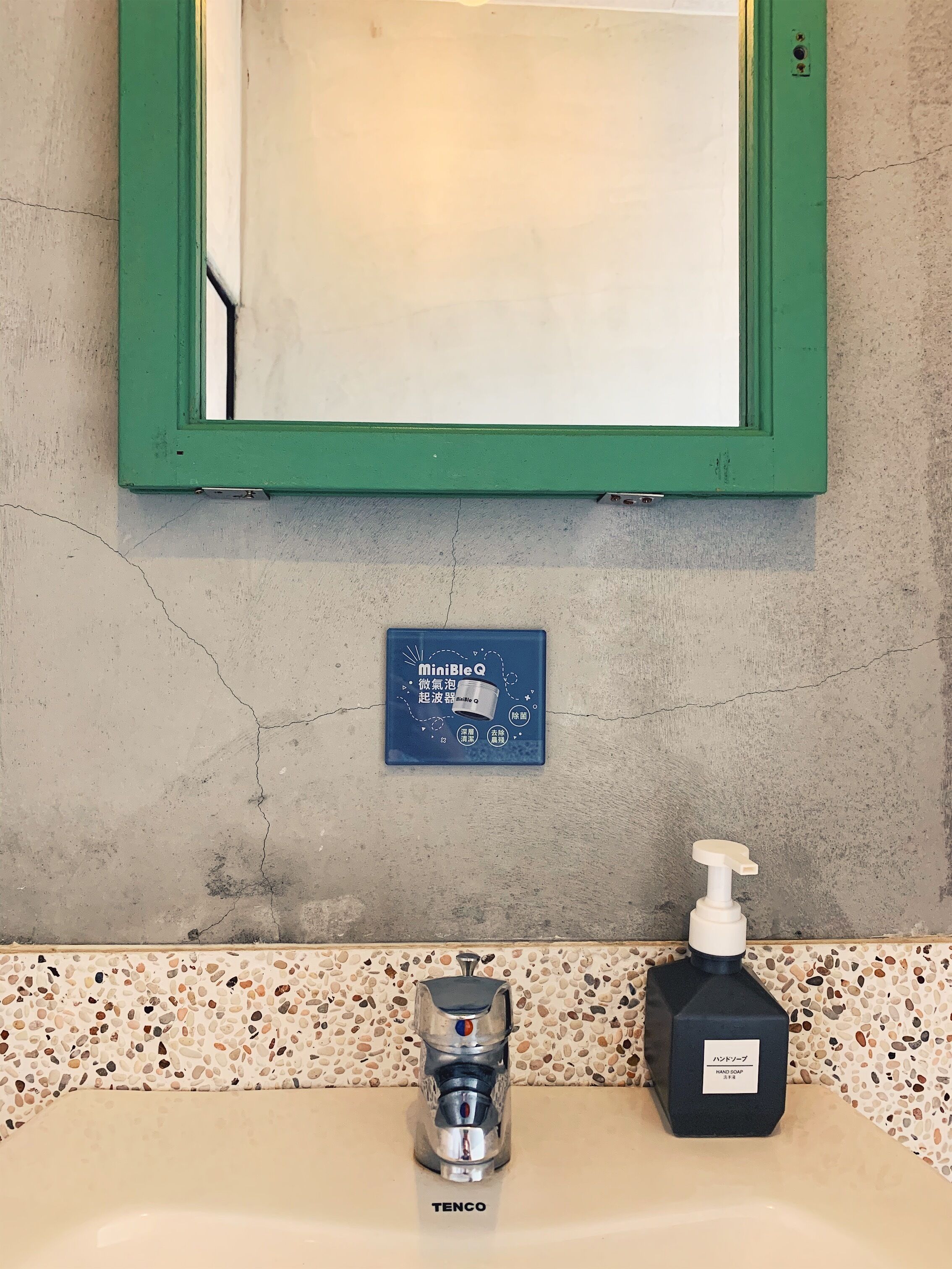 Un baño con un espejo de marco verde, un dispensador de jabón y una fuente de agua.