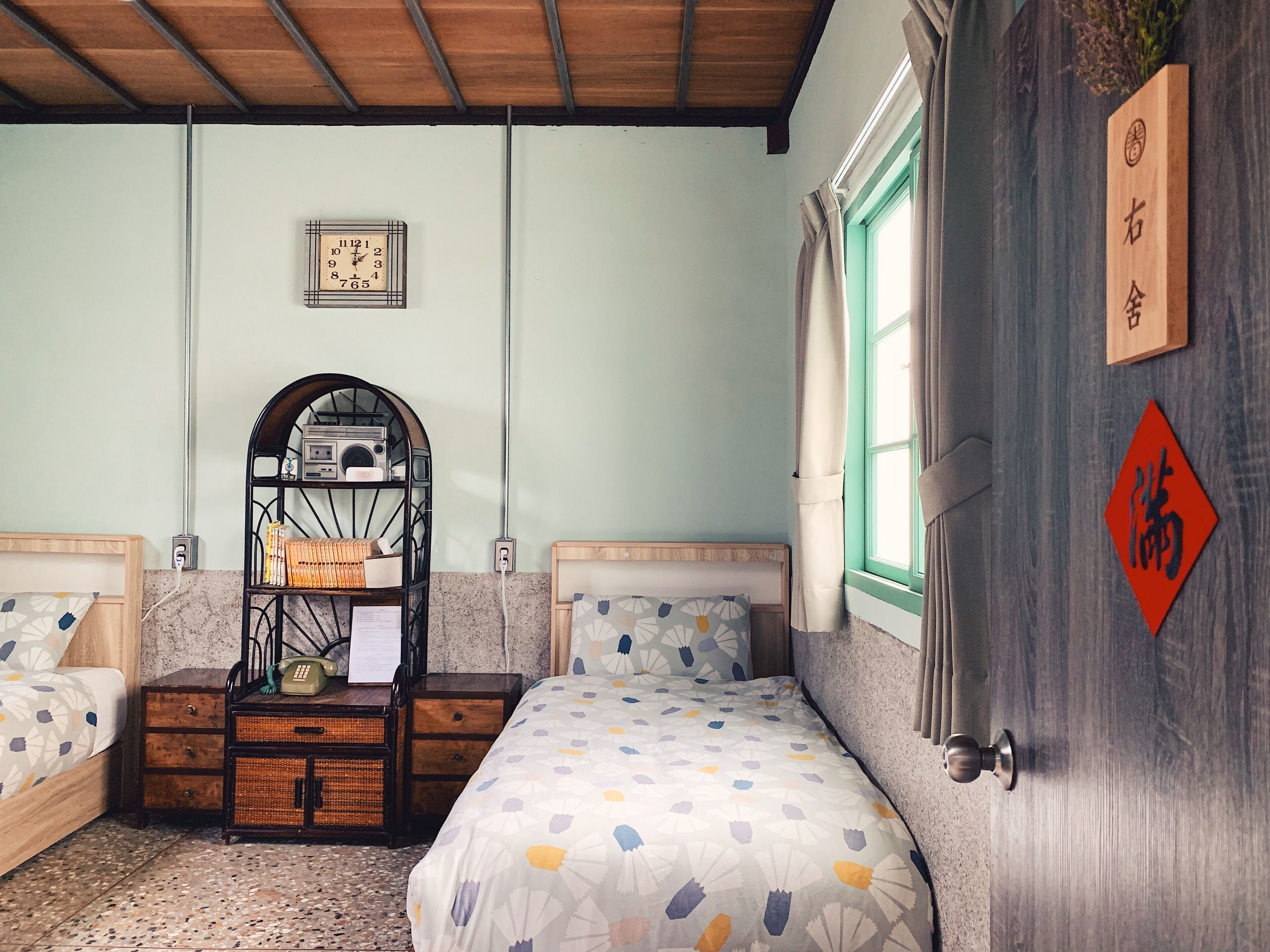 A bedroom with two beds, a radio on a shelf, a clock on the wall, and a wooden door with Chinese characters.