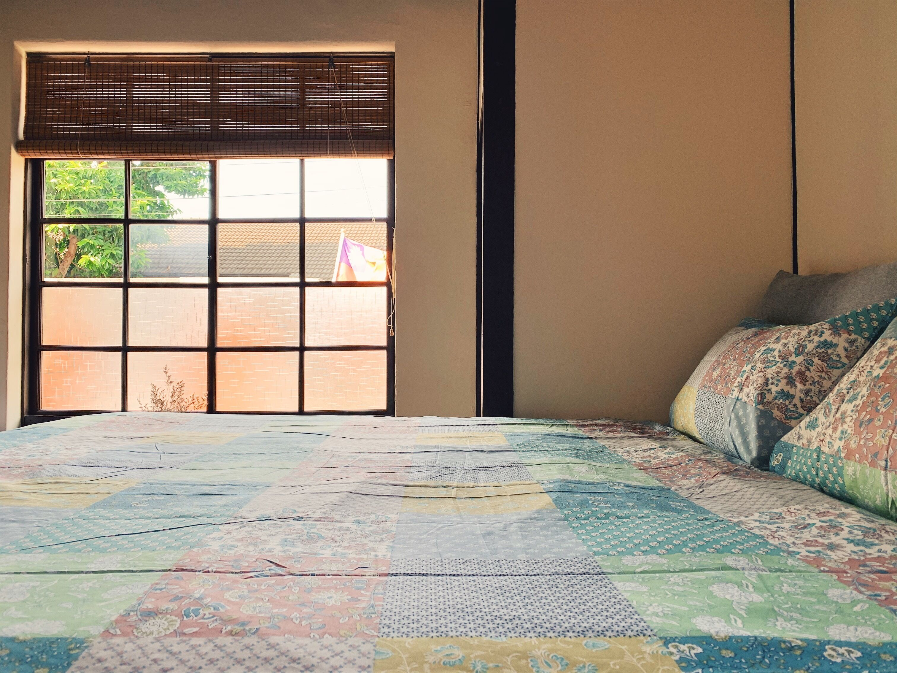 Un dormitorio con un ventanal grande, una cama con un colcha colorida y una estantería de pared.