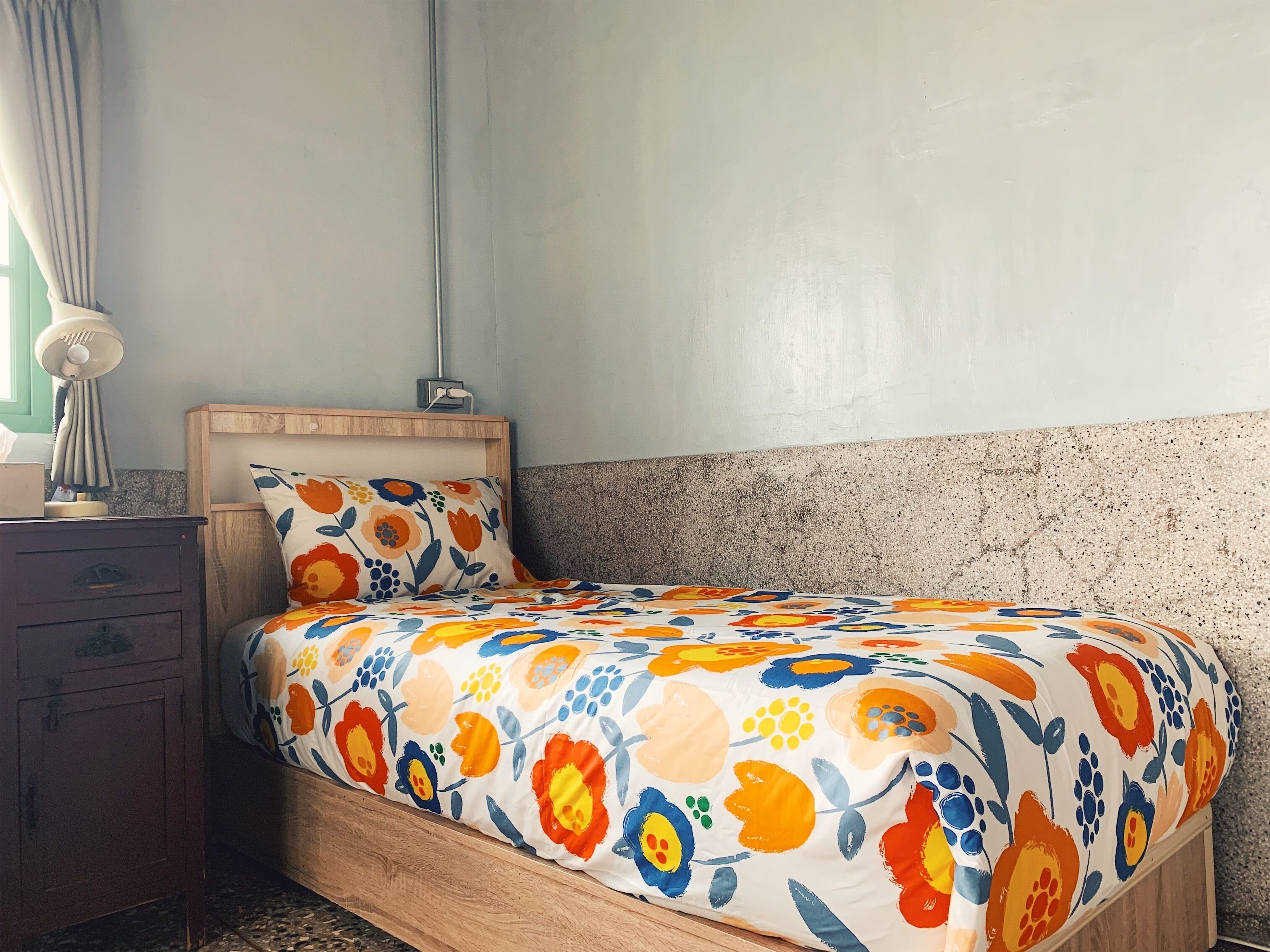 A bed with a colorful floral bedspread, a wooden headboard, and a nightstand with a lamp.