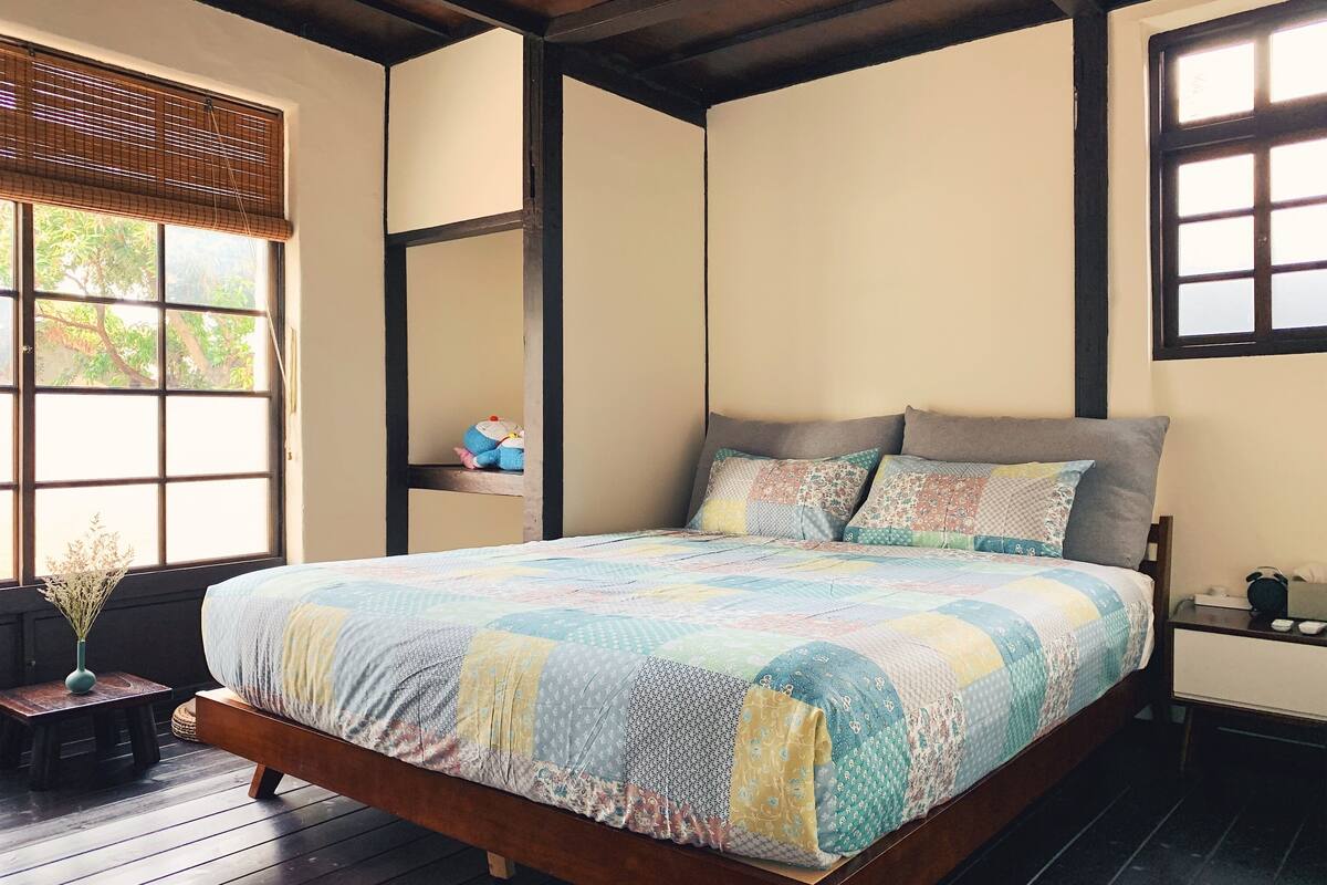 Een slaapkamer met een houten bed, een quilt, een nachtkastje en een raam met jaloezieën.