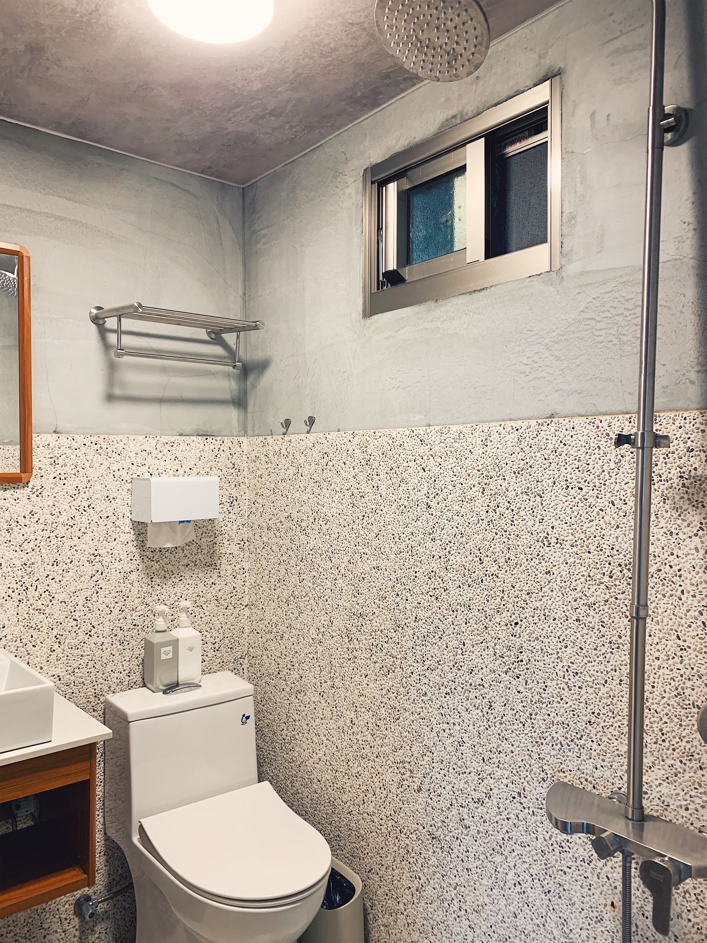 A bathroom with a toilet, a hand dryer, a towel rack, a window, and a shower.