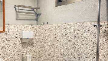 A bathroom with a toilet, a hand dryer, a towel rack, a window, and a shower.