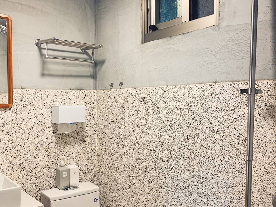 A bathroom with a toilet, a hand dryer, a towel rack, a window, and a shower.
