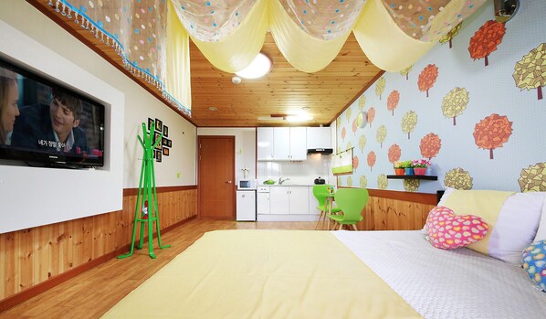 A cozy room with a bed, a TV, a green chair, and a kitchen in the background. - Lake Scenery Pension (Gangneung)