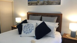 A neatly made bed with a wooden headboard, multiple pillows, and two bedside lamps. - Baden 70 - Rainbow Shores. Ground Floor. Air Con. Overlooking lap pool. Wi-Fi (Rainbow Beach)