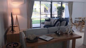 A living room with a sofa, a coffee table, and a dining area with chairs and a table. - Baden 70 - Rainbow Shores. Ground Floor. Air Con. Overlooking lap pool. Wi-Fi (Rainbow Beach)