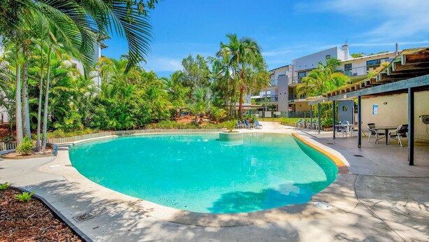A swimming pool surrounded by palm trees and a building with a flat roof. - Baden 70 - Rainbow Shores. Ground Floor. Air Con. Overlooking lap pool. Wi-Fi (Rainbow Beach)