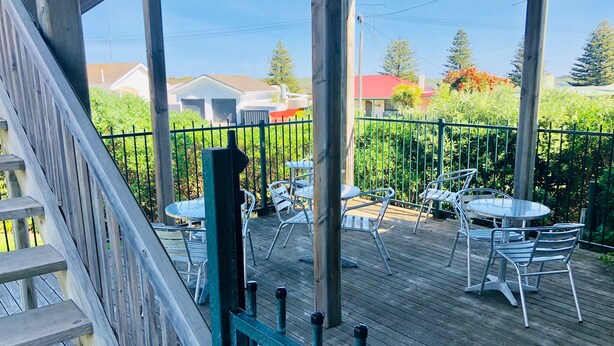 A wooden deck with outdoor seating, a railing, and a view of houses and trees. - Pinehaven Motel (Nelson)