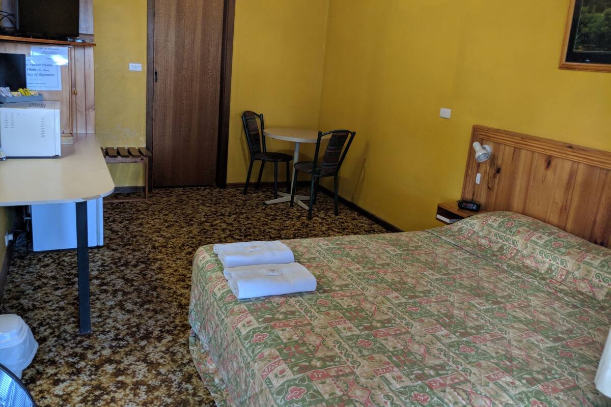 Una habitación de hotel con cama, escritorio con microondas, silla, mesita y puerta.