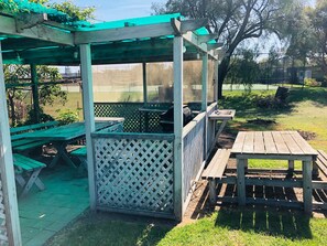 A covered outdoor seating area with picnic tables and a grill. - Pinehaven Motel (Nelson)