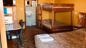A bunk bed with a patterned bedspread, a wooden desk with a chair, a television, and a bathroom visible through an open door. - Pinehaven Motel (Nelson)