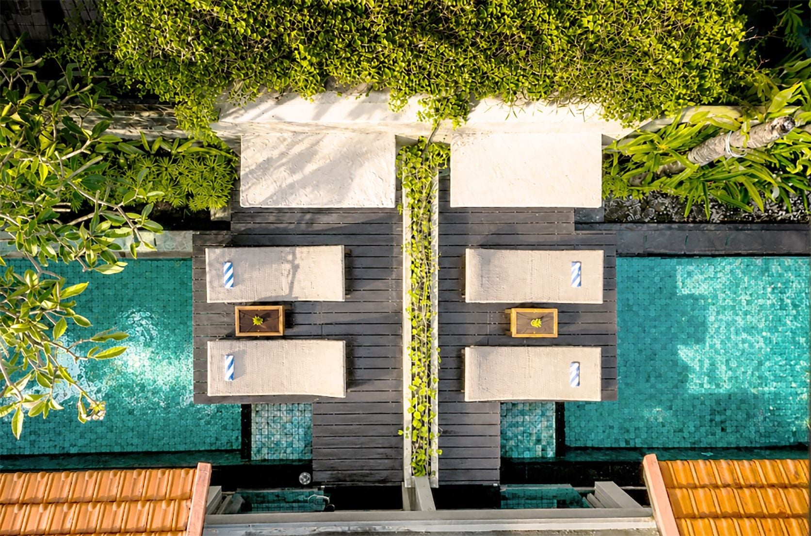 Un espace aménagé au bord de la piscine, comprenant deux coins salon, chacun avec une petite table et une chaise, le tout entouré d’une végétation luxuriante.