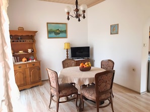 Un coin repas avec une table dressée pour quatre personnes, entourée de chaises à motifs floraux. Un téléviseur est fixé au mur, et un tableau est accroché au-dessus de la table.