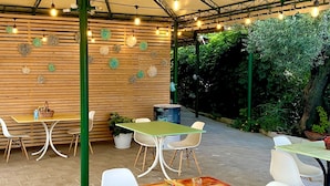An outdoor patio area with wooden tables and white chairs, string lights, and potted plants. - Villa Elisa Apartments (Minturno)
