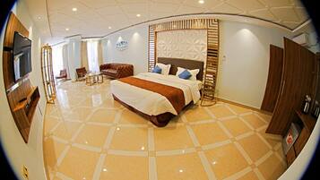 Um quarto espaçoso com uma cama grande, televisão e área de estar com sofá e poltronas.