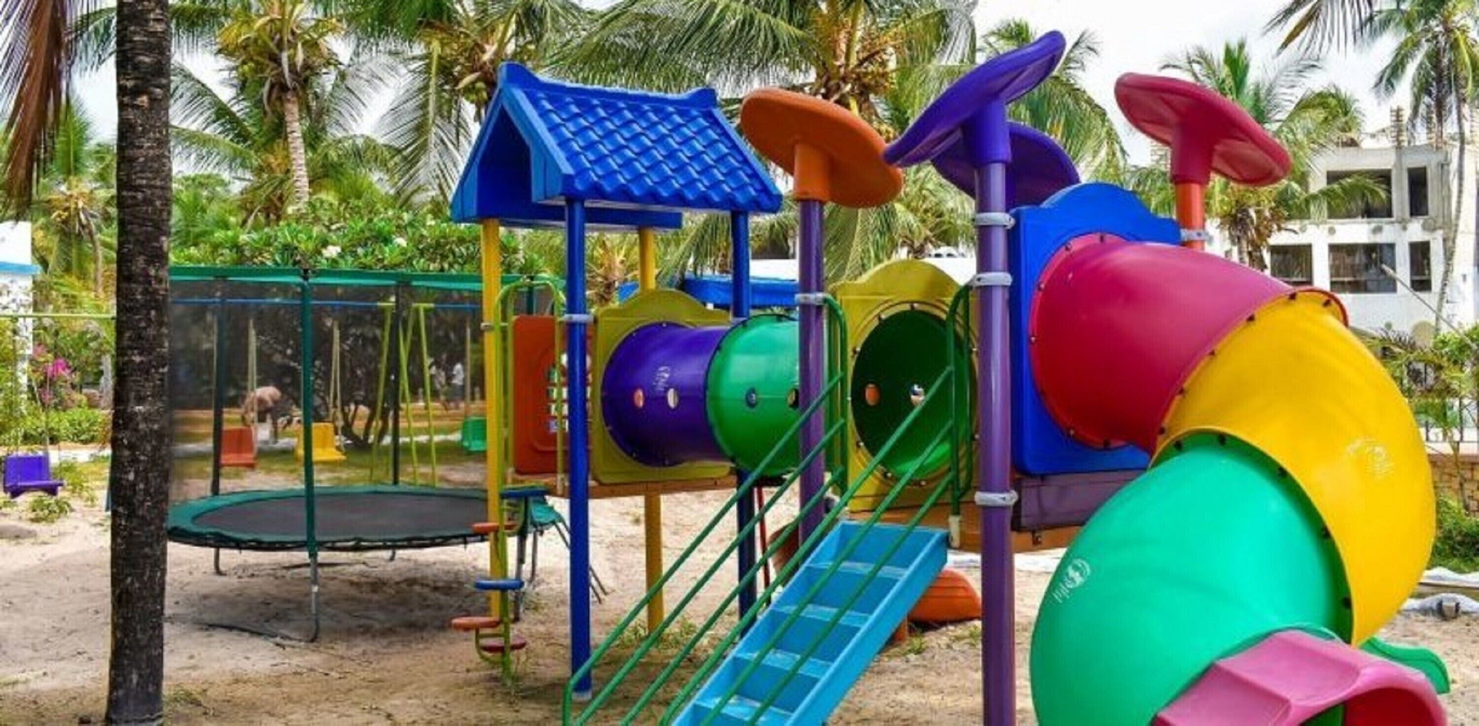 Un parque infantil con tobogán, estructuras para escalar y un trampolín.