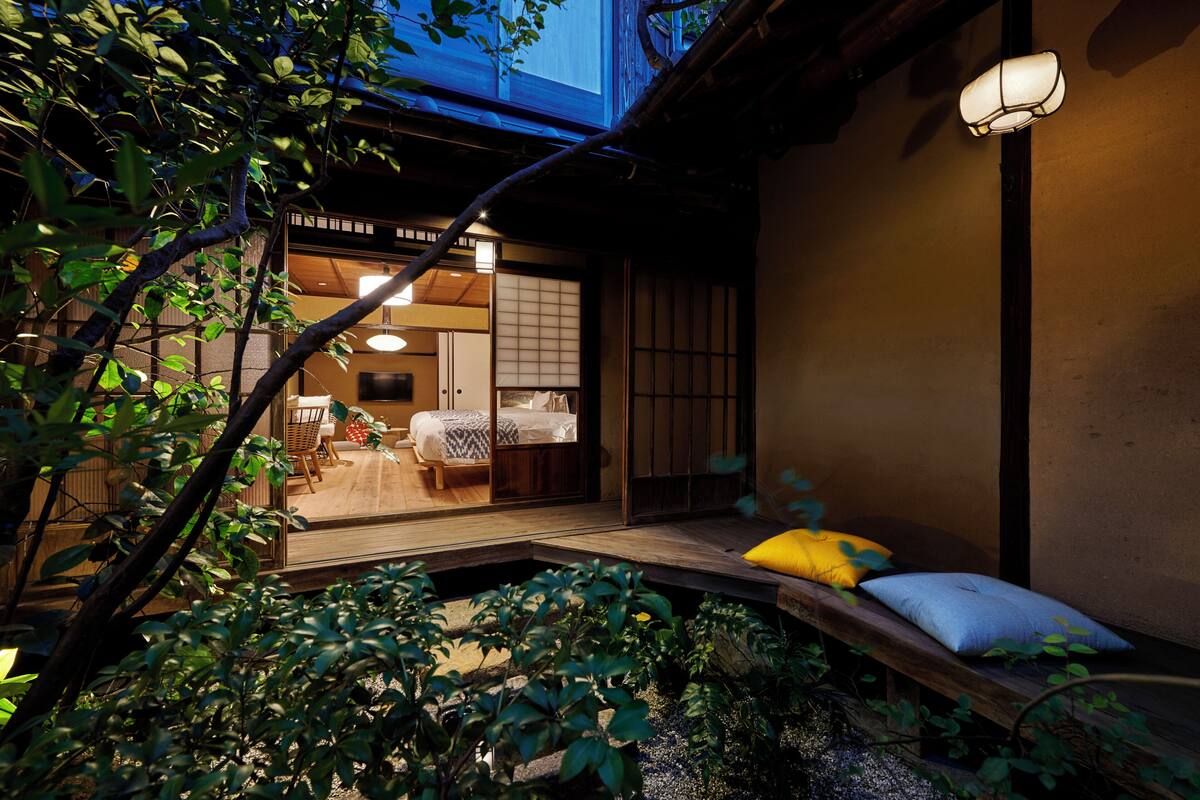 A traditional Japanese-style room with tatami flooring, a low wooden bench with cushions, and a sliding door leading to a washbasin area.