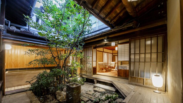 Une cour de style japonais traditionnel, avec un plancher en bois, un petit arbre et une lanterne en pierre.