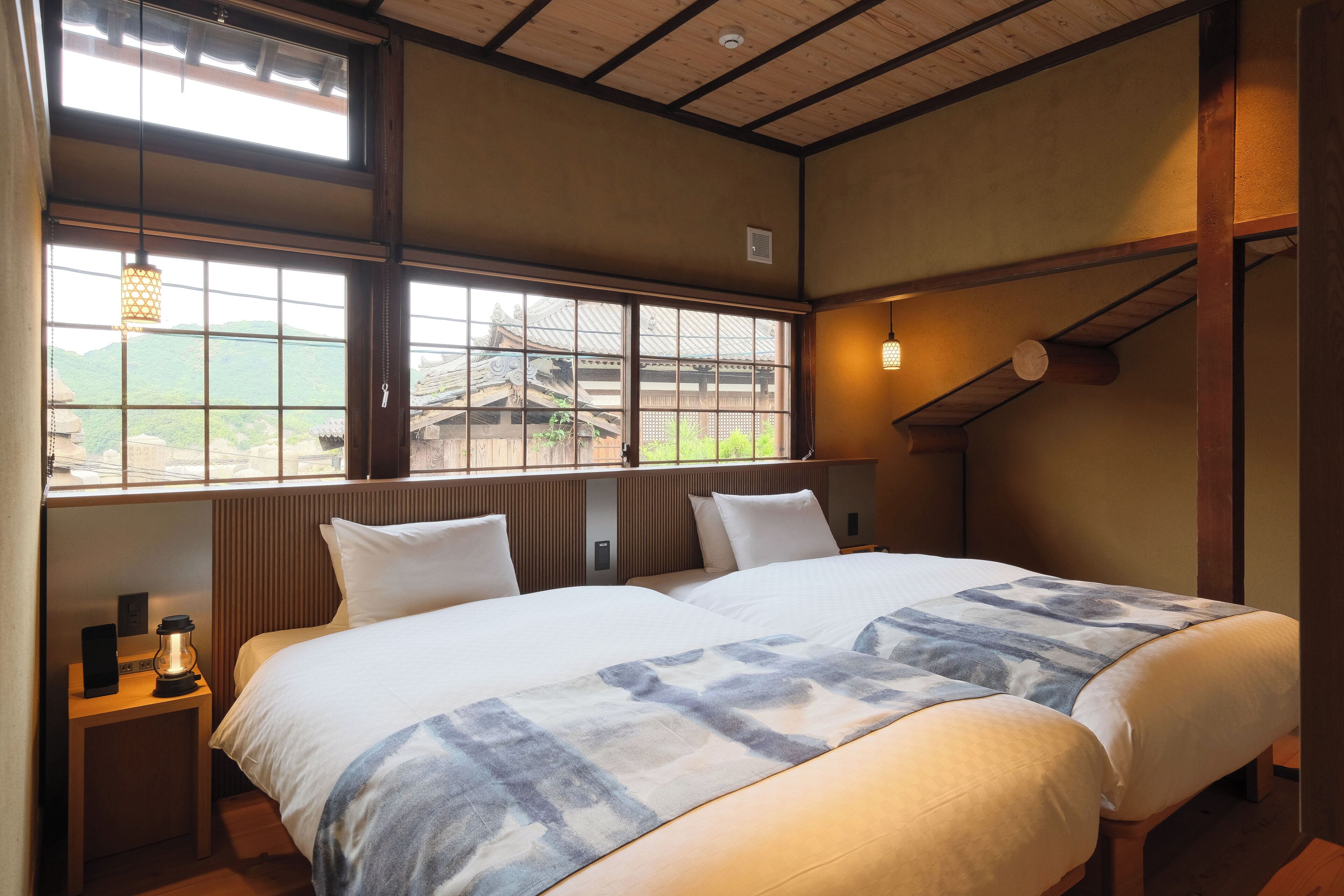Ett hotellrum med två sängar, utsikt över en traditionell byggnad och ett träpanelat tak.