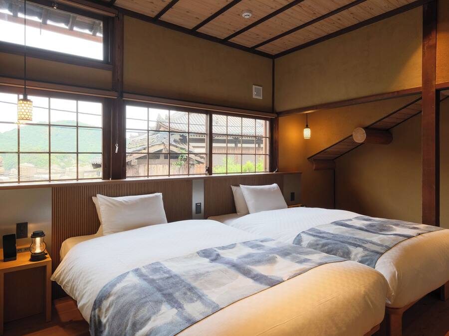A hotel room with two beds, a view of a traditional building, and a wooden ceiling.