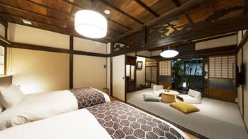 Ein traditioneller japanischer Raum mit Tatami-Bodenbelag, niedriger Holzdecke und Schiebetüren. Zwei Betten mit gemusterten Bettwäsche sowie eine kleine Sitzecke mit Kissen sind vorhanden.