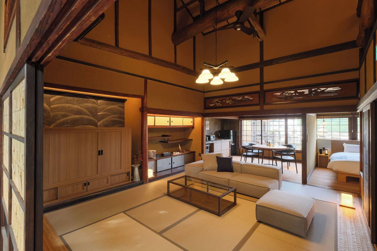 A traditional Japanese-style room with tatami flooring, a low wooden table, a sofa, and a bed.