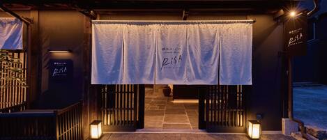 A hotel entrance with a covered walkway, illuminated by wall-mounted lights, and a banner displaying the hotel's name.