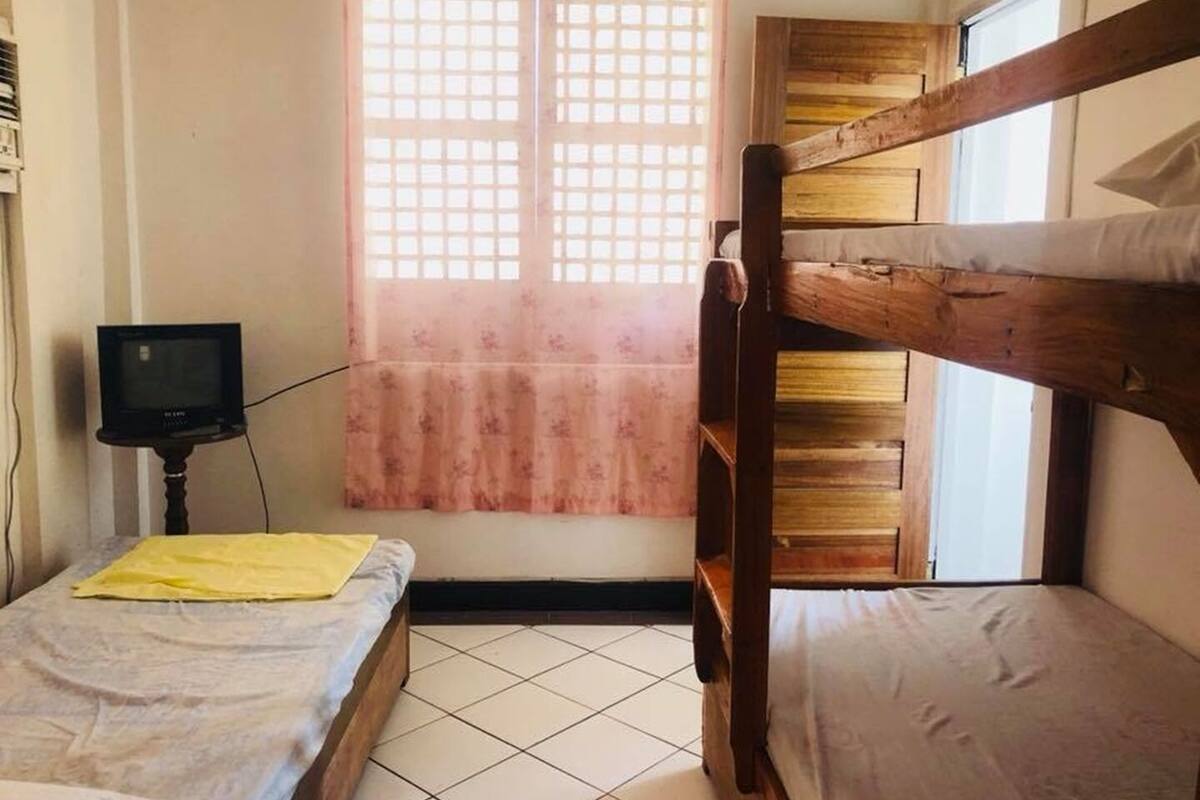 A room with a bunk bed, a small table with a television, and a window with a floral curtain.