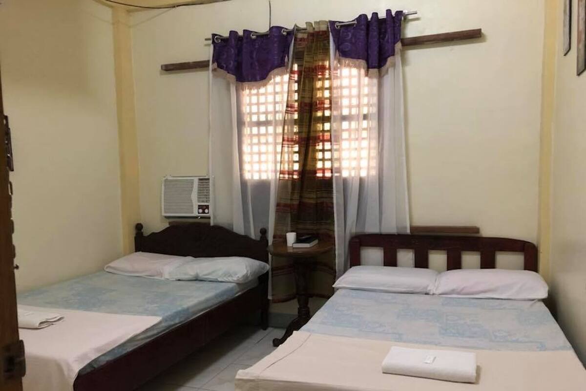 A room with two single beds, a small table, a chair, and a window with curtains.