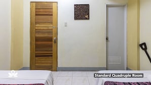 A standard quadruple room with two beds, a wooden door, a small wall decoration, and a broom leaning against the wall. - Coffee Swings Lodging House (Vigan)