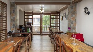 A dining area with wooden tables and chairs, a view of the outdoors through a glass door, and a stone wall with a lantern. - Coffee Swings Lodging House (Vigan)