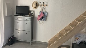 Ein Waschbereich mit Waschmaschine, einem Fernseher auf einem Schrank, einem Kleiderständer mit Hüten und einer Tasche auf dem Boden.