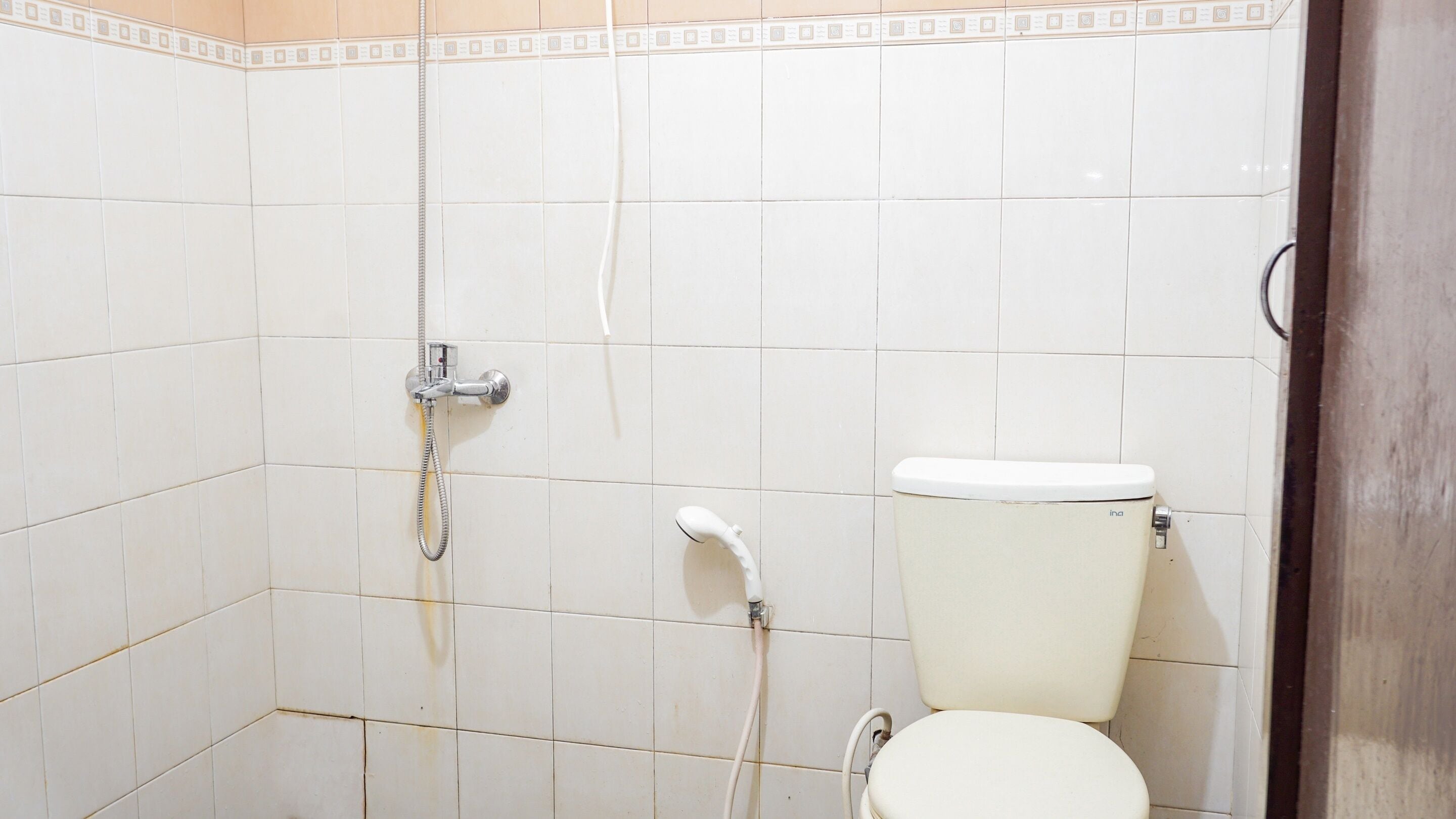 A bathroom with white tiled walls, a toilet, and a shower with a handheld showerhead.