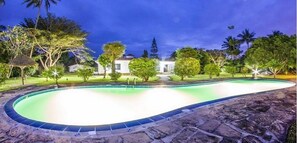 A swimming pool with a curved edge, surrounded by a stone deck and lush greenery. - Olive House (Mtwapa)