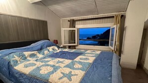 Un dormitorio con una cama grande, una ventana con vista al mar y un cabecero.