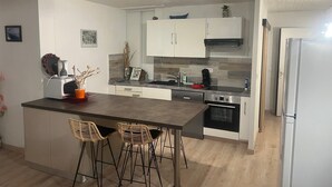 Una cocina moderna con una isla central, dos taburetes de bar, armarios blancos y electrodomésticos de acero inoxidable.